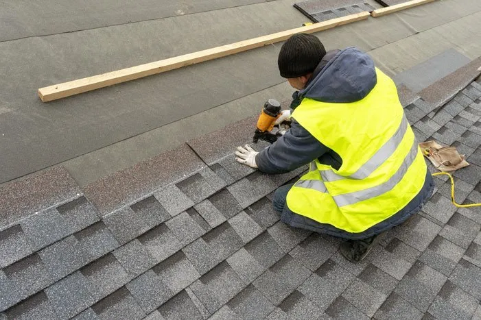 Man completing a new roof replacement installation with shingles