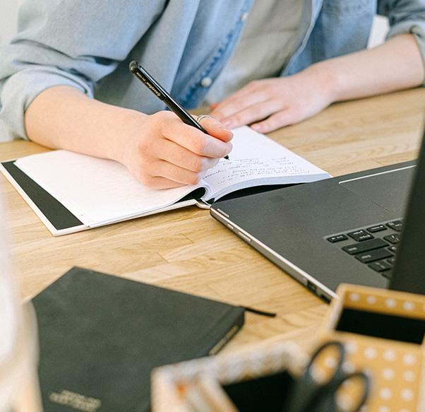 man writing in notepad at desk